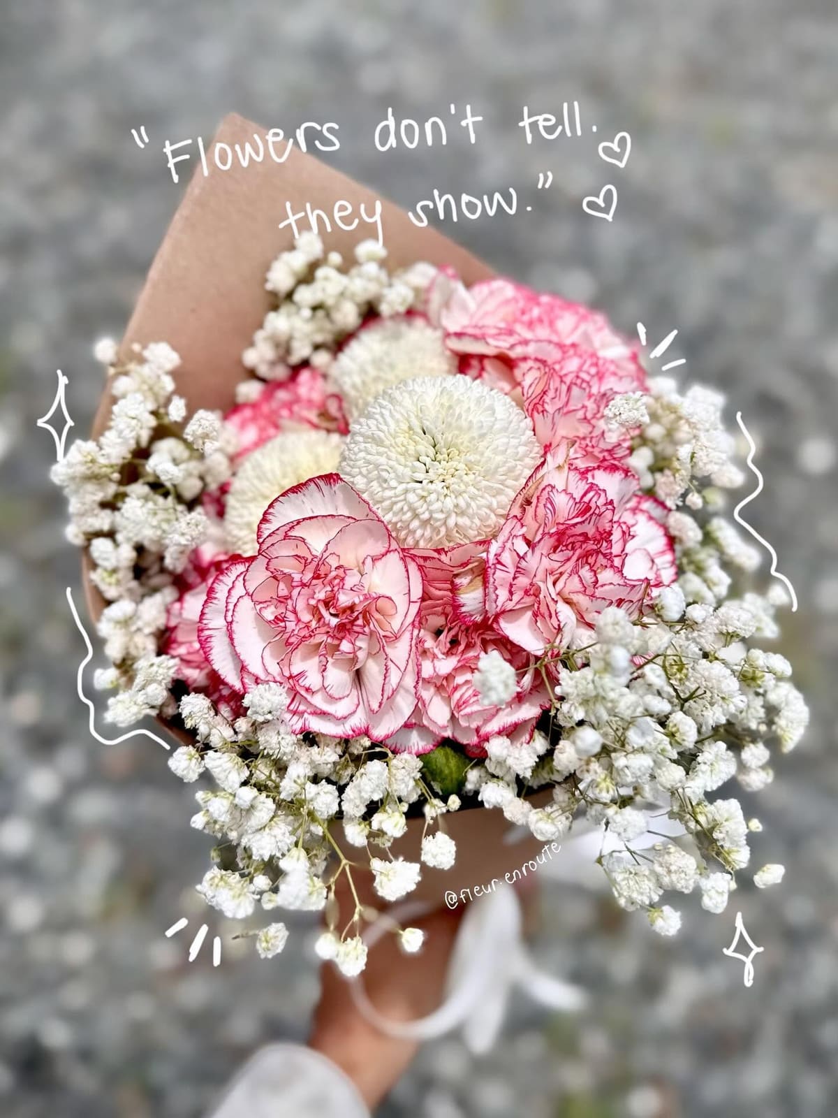 Pink-edged carnations and baby's breath bouquet held over grey pavement