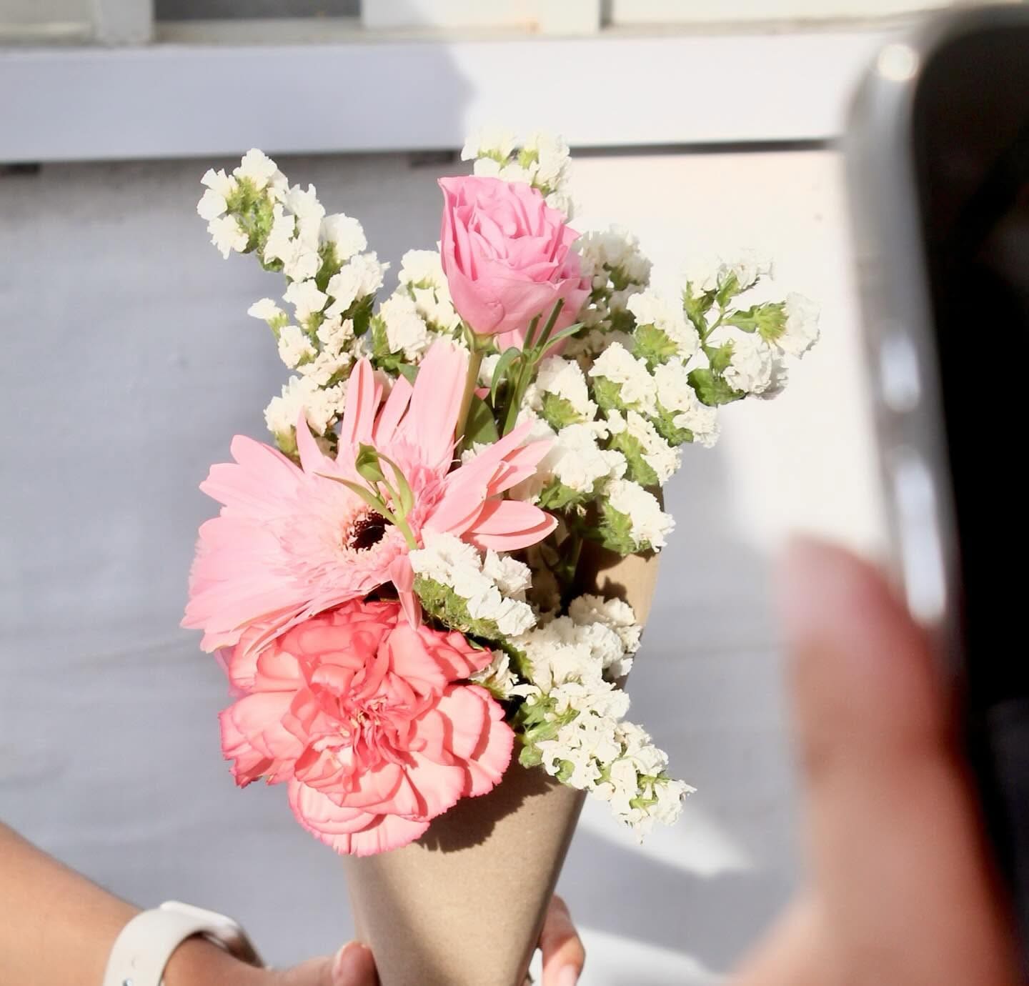 A kraft cone bouquet of pink carnations and a gerbera being handed to a customer in golden light