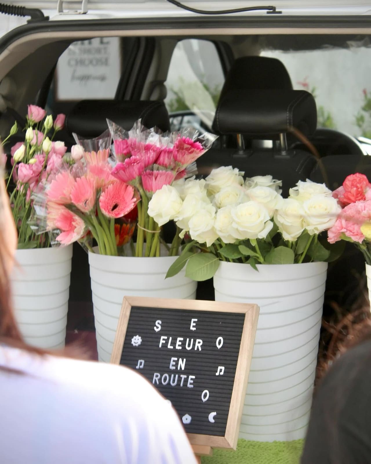 The Fleur en Route trunk: buckets of pink gerberas and white roses behind a letterboard