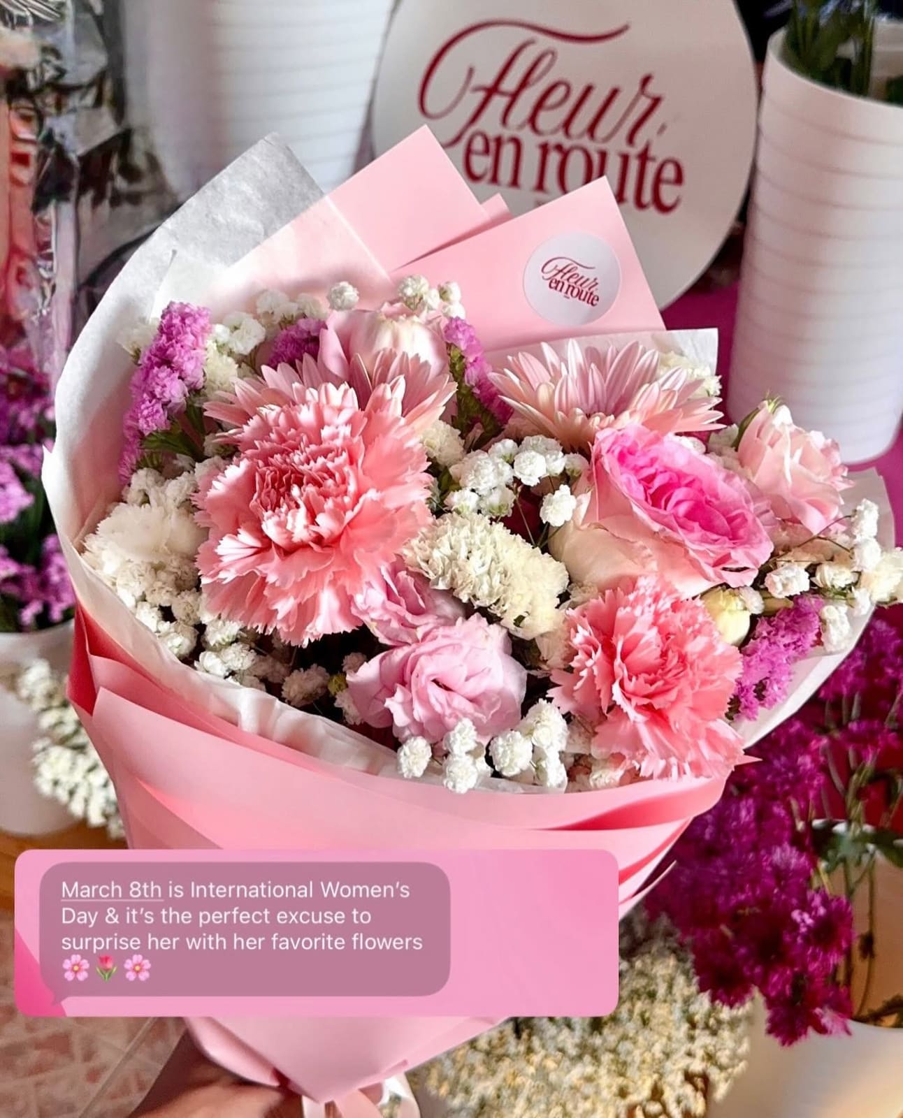 Pink bouquet in pink wrapping beside the round Fleur en Route board