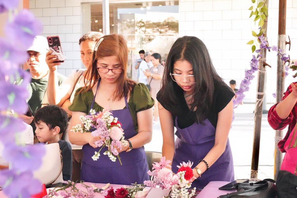 Guests in purple aprons arranging pink and lilac flowers at a workshop table