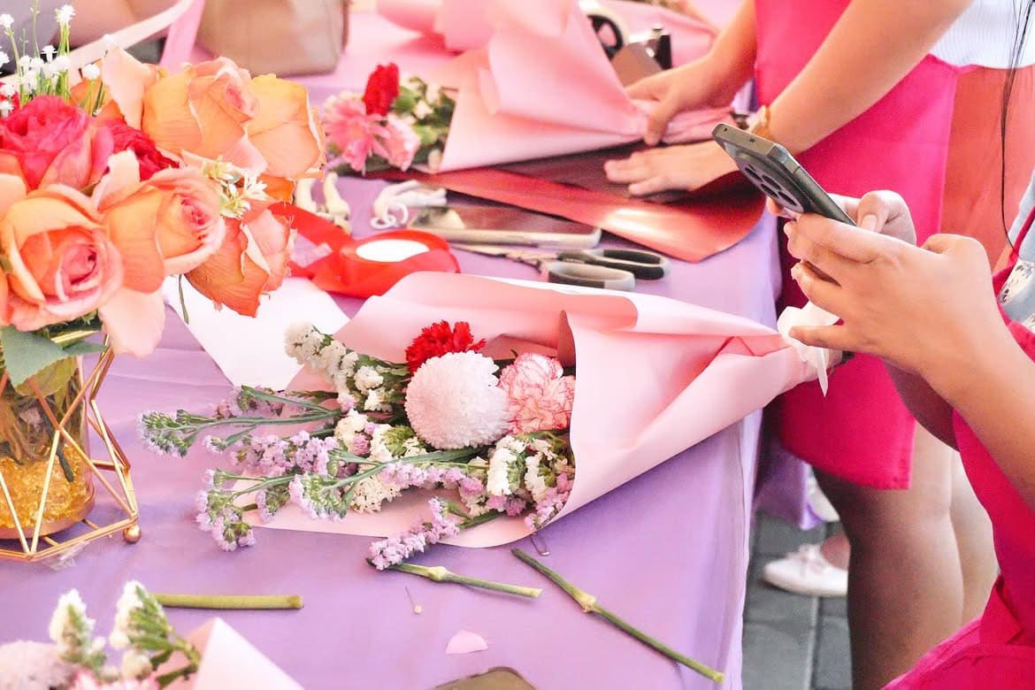 Workshop table with peach roses, ribbons, scissors, and pink wrapping paper